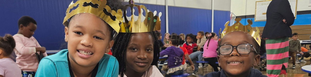 Three kids wearing gold paper crowns sitting at a table.